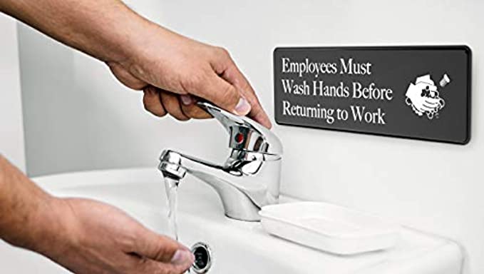 Close-up of an 'Employees Must Wash Hands' sign in use next to a sink, ensuring hygiene standards are met.