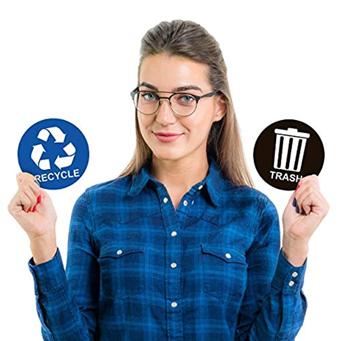 A woman holding a blue recycle sticker in one hand and a black trash sticker in the other, demonstrating the size and design of the stickers