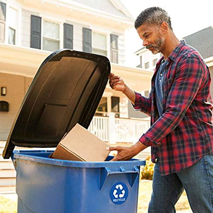 A man placing a cardboard box into a recycling bin with a blue recycle sticker prominently displayed, illustrating the sticker's use on outdoor bins