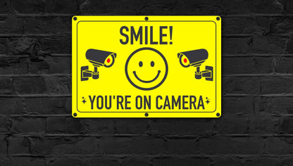 Smile You're On Camera Sign mounted on a black brick wall, providing a strong visual deterrent against theft and vandalism. 