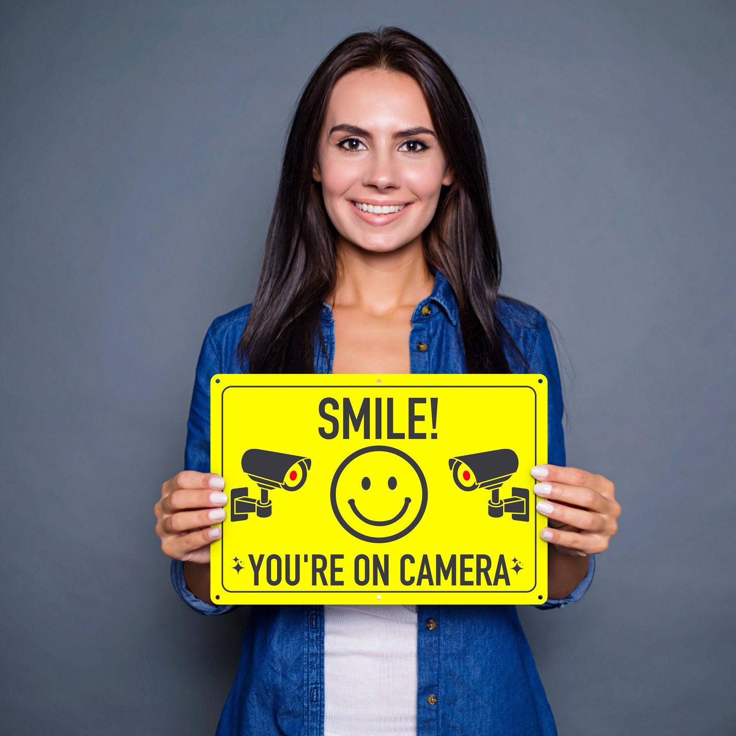 Woman holding Smile You're On Camera Aluminum Sign, showcasing its sturdy design and clear visibility for use in any setting